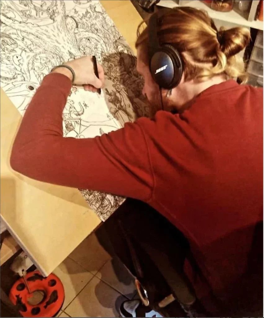 Davy Crow, illustrateur en Alsace, dessine à l'encre noire, casque sur les oreilles, dans son atelier de Brumath